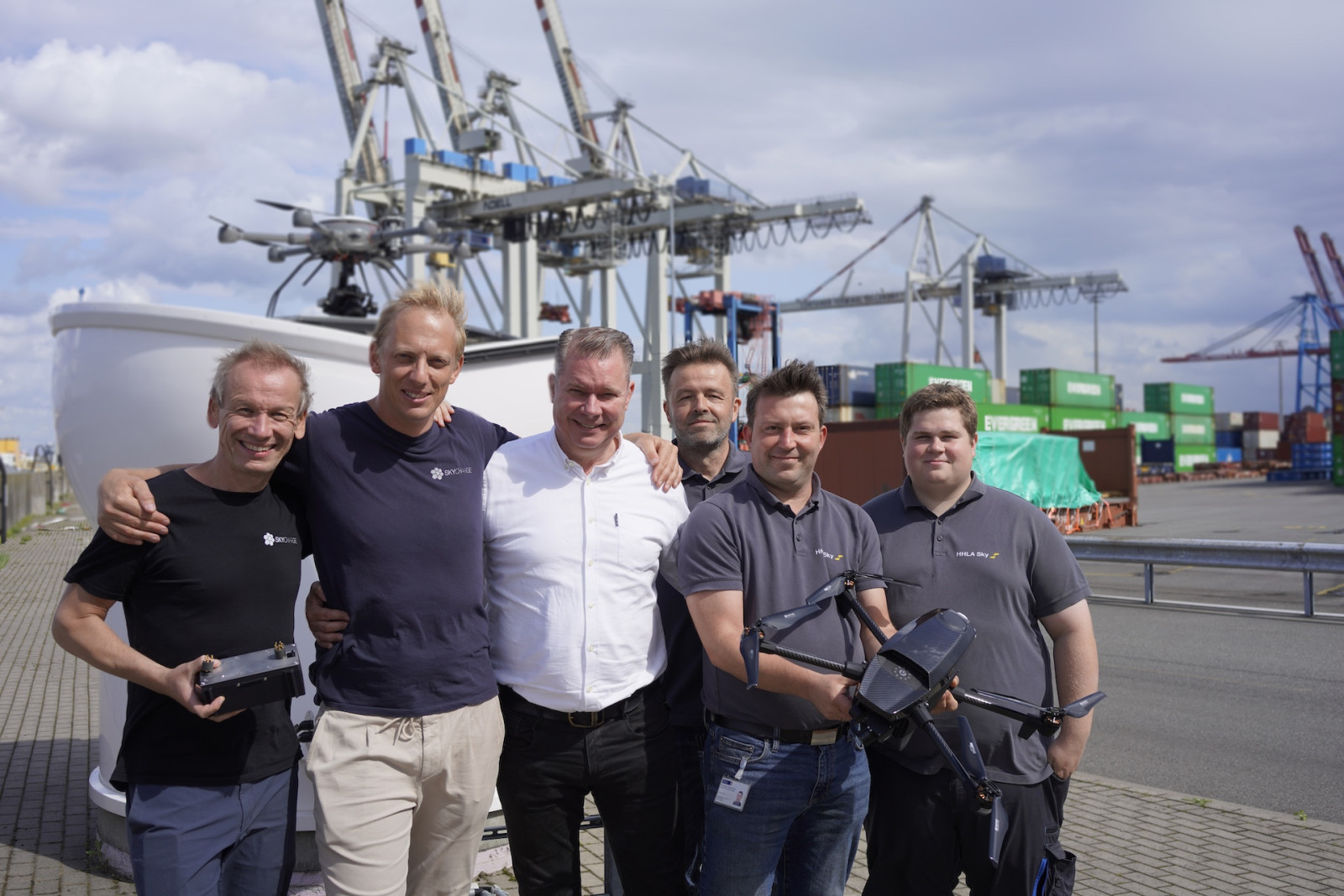 Group of 6 standing in front of port cranes with a drone